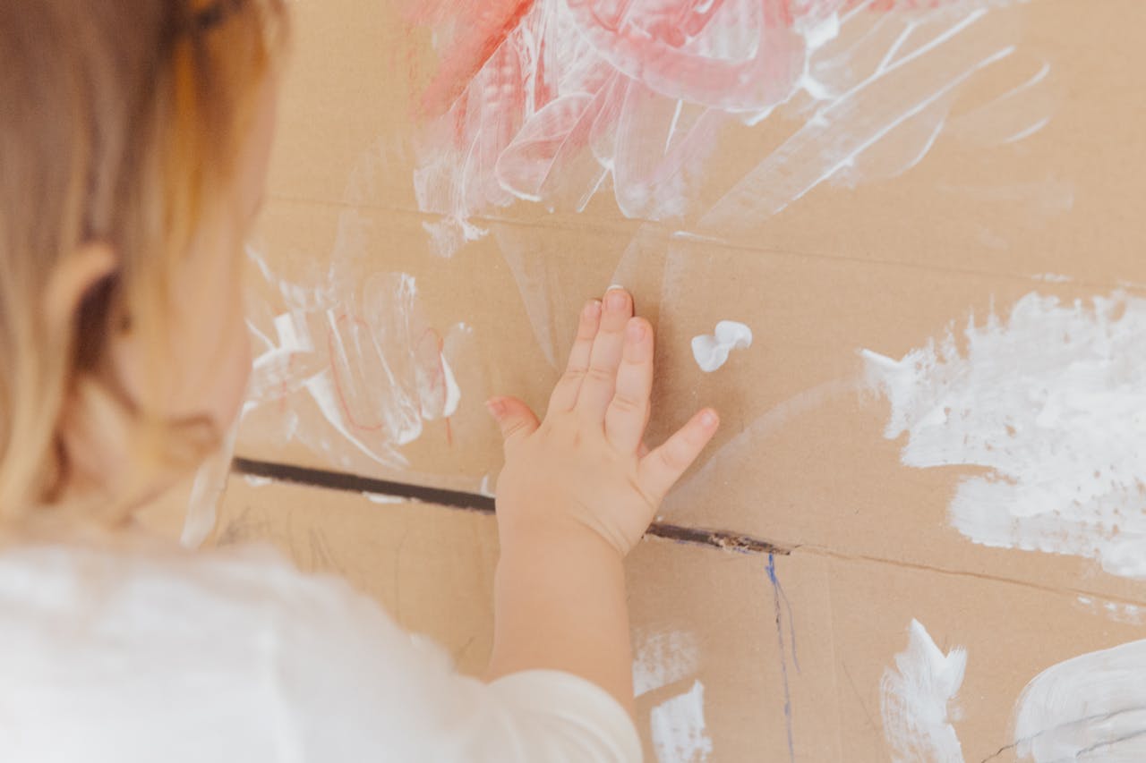 Crop anonymous child drawing with white paint at home